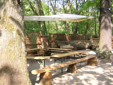 Rustikale Sitzecke im Waldbiergarten mit Bierbänken, Sonnenschirm und Bäumen